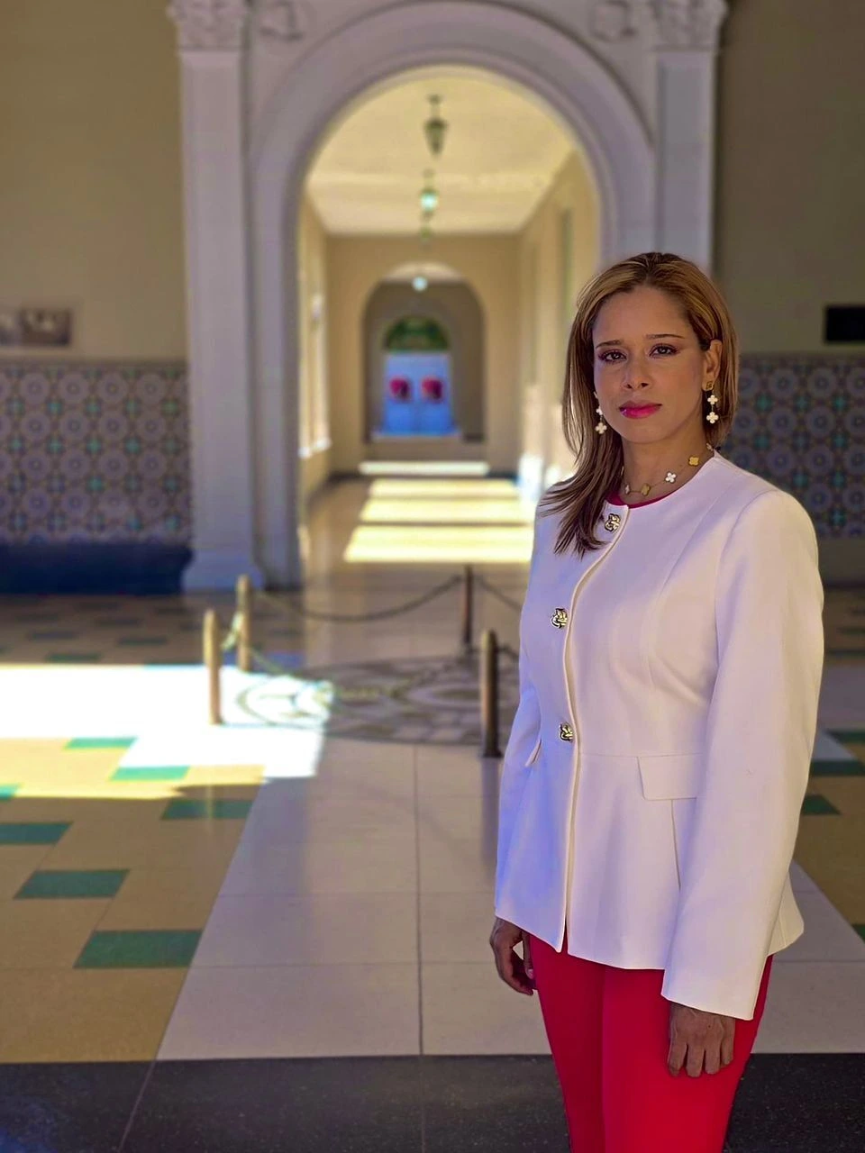 Zoraida Cruz dressed in a white blazer stands in a modern hallway